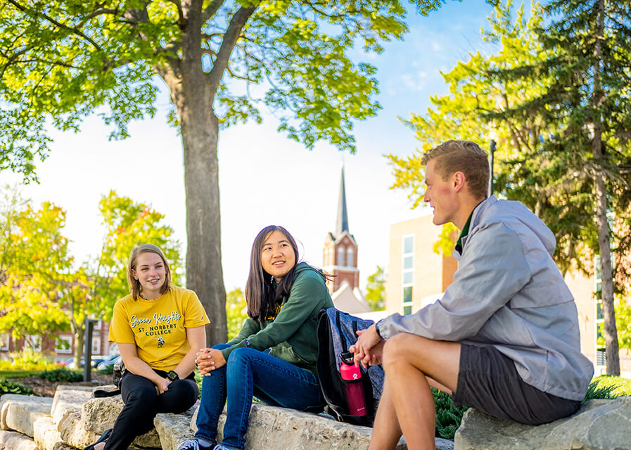 Three students talking with St. Joseph Parish in the background